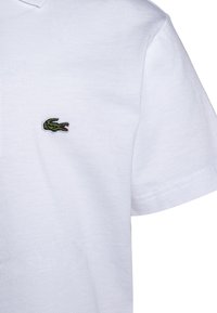 Biała bawełniana koszulka polo z zielonym haftowanym logo krokodyla na lewej stronie klatki piersiowej. Krótkie rękawy z klasycznym kołnierzykiem.