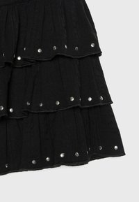 Tissu noir à étages avec des clou en métal argenté le long des bords, montrant un matériau texturé et un design en couches.