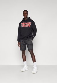 Fekete kapucnis pulóver "Chicago Bulls" grafikával, fekete hálós sorttal párosítva. Fehér sportcipő és zokni egészíti ki az öltözetet.