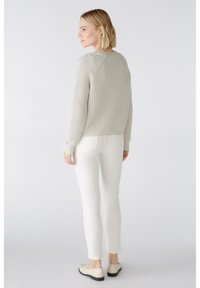 Hellgrauer, gestrickter Pullover mit gerippter Textur, kombiniert mit eng anliegenden weißen Jeans und beigen Slippers. Schlichtes Design, keine sichtbaren Muster.