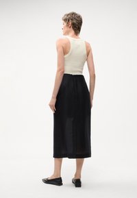 Czarna, sięgająca kostek spódnica z lekkiego materiału, z zamkiem błyskawicznym z tyłu. Połączona z dopasowanym beżowym topem na ramiączkach i butami na niskim obcasie.