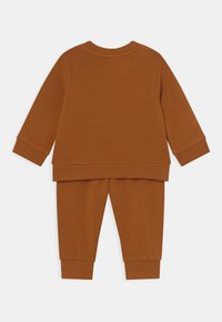 Orange-brun bomullshoodie och matchande byxor. Stretchiga muddar och nederkant med en mjuk, slät textur. Enkel, avslappnad design utan mönster.