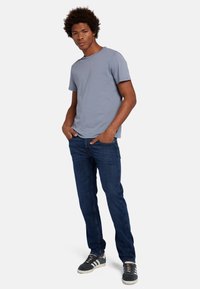 T-shirt grigia a collo rotondo, jeans slim-fit blu scuro e sneaker nere con suola bianca. Outfit casual con un design rilassato.