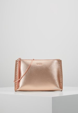 Metaliczna kopertówka z różowego złota ze skóry z wąskim paskiem i subtelnym wytłoczonym logo marki na gładkiej białej powierzchni.