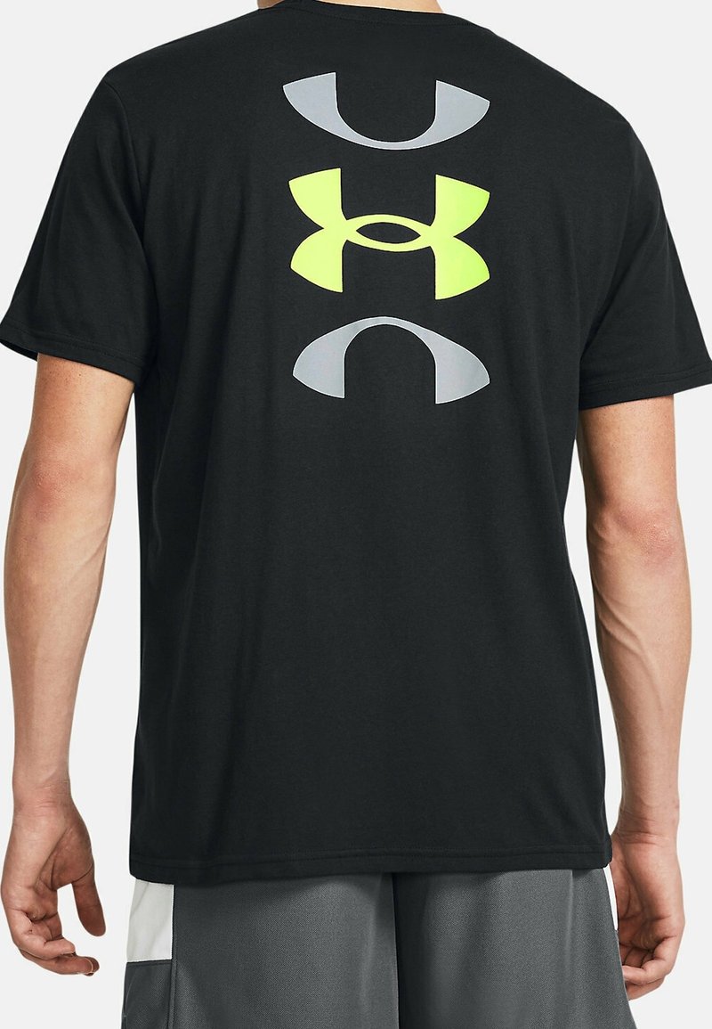 Camiseta negra de manga corta con grandes logotipos de Under Armour en amarillo y gris impresos verticalmente en la parte trasera. Tejido suave de algodón.