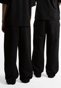 Schwarze, übergroße T-Shirts, kombiniert mit locker sitzenden schwarzen Sweatpants, die eine glatte Textur aufweisen und keine sichtbaren Muster oder Akzente haben.