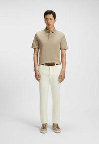 Beige polo shirt with four buttons, paired with white trousers and beige sneakers. Smooth fabric and tailored fit; minimal design.