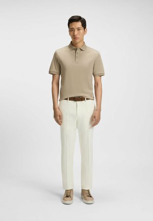 Beige polo shirt med fire knapper, parret med hvide bukser og beige sneakers. Glat stof og skræddersyet pasform; minimalistisk design.