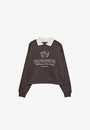 Mørkebrunt cropped sweatshirts med hvid polo-krave og hvid tekst foran samt hesteplejer-emblem, hvor der står "Polo Training Co. Udfordr dine grænser hver dag."