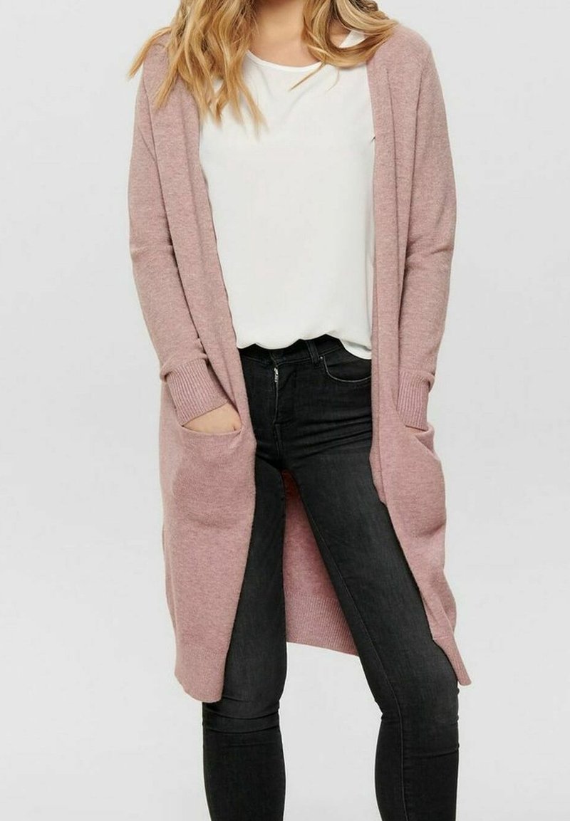 Cardigan lungo rosa chiaro realizzato in morbido materiale a maglia, con due tasche frontali, design aperto e polsini a coste. Abbinato a jeans neri.