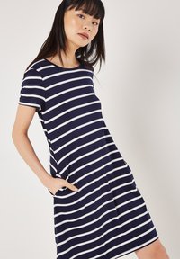 Marineblaues Kleid mit horizontalen weißen Streifen, kurzen Ärmeln, rundem Ausschnitt und seitlichen Taschen. Weicher Stoff mit lockerer Passform.