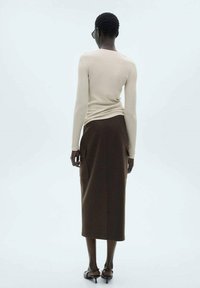 Langärmliges beiges Rippoberteil, kombiniert mit einem dunkelbraunen, hochgeschnittenen Midirock mit seitlichen Taschen und glatter Textur.