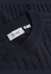 Granatowy sweter z żebrowanym wzorem, okrągłym dekoltem i naszytą metką z napisem "LES DEUX" oraz etykietą rozmiaru. Wykonany z dzianinowego materiału.