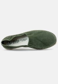 Zielony pantofel wykonany w 100% z organicznej bawełny, z teksturowaną powierzchnią, kontrastowym przeszyciem i szczegółami z naturalnych włókien w podeszwie.