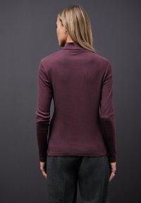 Maglia a maniche lunghe, aderente, in tessuto ribbed di un profondo bordeaux, con un collo alto e texture liscia, abbinata a pantaloni grigio scuro.