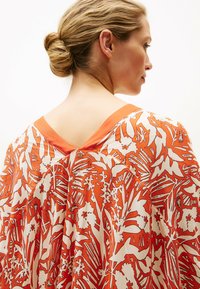 Abito arancione con motivo floreale e scollatura posteriore a V, caratterizzato da un tessuto leggero e un design fluido. Decorato con stampe botaniche bianche.