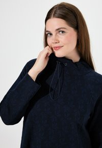 Pullover blu navy con motivo a foglia texturizzato, colletto alto e coulisse regolabile. Realizzato in tessuto morbido con maniche lunghe.