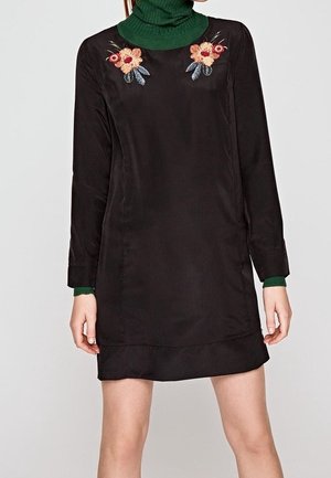 Schwarzes Kleid aus Satin, mit langen Ärmeln und rundem Ausschnitt, verziert mit floralem Stickerei auf der Brust und einem strukturierten grünen Rollkragen.