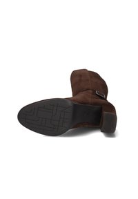 Brown suede ankle boot with a rounded toe, low block heel, and a textured rubber sole. Features a decorative side buckle detail.