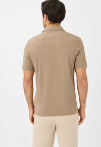 Polo shirt marrone a maniche corte con colletto classico, texture liscia e dettagli cuciti sulle spalle e sull'orlo.