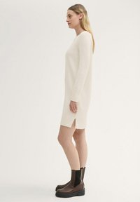 Strickkleid in Creme mit gerippten Bündchen und seitlichen Schlitzen, kombiniert mit braunen Leder-Ankle-Boots mit elastischen Einsätzen und dicken Sohlen.