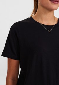 Černé bavlněné tričko s krátkým rukávem a kulatým výstřihem. Má hladkou texturu, minimalistický design a jemné padnutí kolem krku.