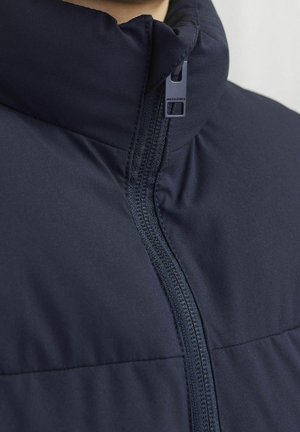 Dunkelblaue gepolsterte Jacke mit hohem Kragen, zentralem Reißverschluss und strukturiertem Stoff mit Nahtdetails für Dämmung und Wärme.