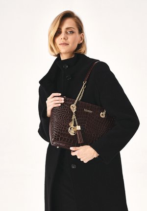 Sac à main en cuir sculpté crocodile marron avec des accents en chaîne, un détail à frange et des accessoires en métal. Texture douce avec une forme structurée.