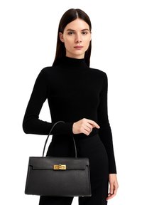 Zwarte leren handtas met een gestructureerde vorm, top handvat en gouden hardware. Het model draagt een aansluitende zwarte coltrui.