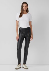 Czarne legginsy z faux skóry o wysokim stanie, zestawione z dopasowaną białą koszulką i beżowymi trampkami. Gładka faktura, elegancki design.