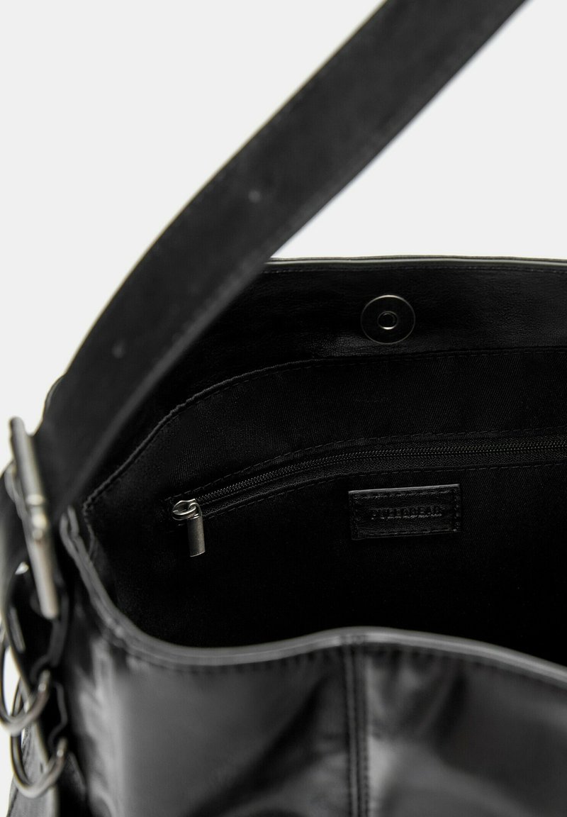 Bolso de mano de cuero negro con textura suave, que cuenta con un bolsillo interior con cremallera, herrajes metálicos y una correa robusta. El interior está forrado en tela negra.
