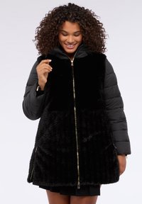 Abrigo acolchado negro con frente de piel sintética, cremallera dorada y bolsillos laterales. Cuenta con mangas acolchadas y capucha, que ofrecen calidez y contraste de texturas.