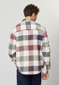Geruite flanellen shirt in rood, groen en wit. Knopfsluitingen bij de mouwen en een afgeronde zoom. Heeft een achterpand met een knoopdetail.
