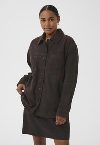 Braune Wildlederjacke mit Kragen, Knopfverschluss, zwei Brusttaschen und langen Ärmeln. Glatte Textur, lockere Passform, mittellang.