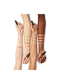 Groupe de bras aux teintes de peau variées affichant des nuances de maquillage. Chaque bras possède une étiquette de couleur et un produit assorti en main.