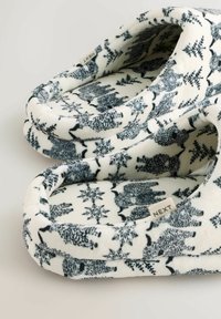 Fleece sloffen met een witte achtergrond en marineblauwe dieren- en sneeuwvlokpatronen. Zachte textuur en gewatteerde randen voor comfort.