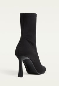 Bottines en tissu extensible noir avec un haut talon aiguille. Présentent un design élégant, une construction sans couture et une base de talon proéminente.