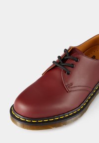 Bordeaux leren schoen met zwarte veters, ronde neus en een gele gestikte zool. Soepele textuur en contrasterende binnenvoering.
