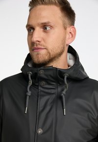 Sort vandtæt jakke med høj krave, grå snore og trykknapper. Glat tekstur, inkluderer en blød grå foring.