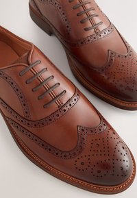 Chaussures habillées en cuir marron avec un design à bout à ailettes, perforations décoratives et un bout lisse. Fermeture à lacets et semelle en caoutchouc.