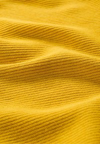 Gul ribbad tyg visar en texturerad yta med parallella linjer som reflekterar ljus och skapar subtila skuggor över materialet.