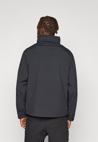 Black waterproof jacket with a high collar and long sleeves. Features a seamless back design without visible fastenings or logos.