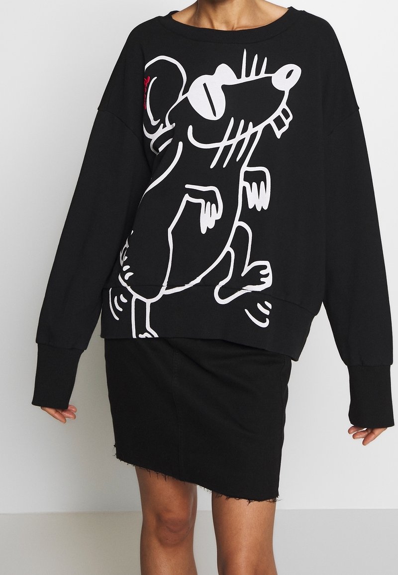 Sudadera negra con gráfico de ratón de dibujos animados blanco, corte oversized, escote ancho y puños acanalados. Combinada con una falda vaquera negra.