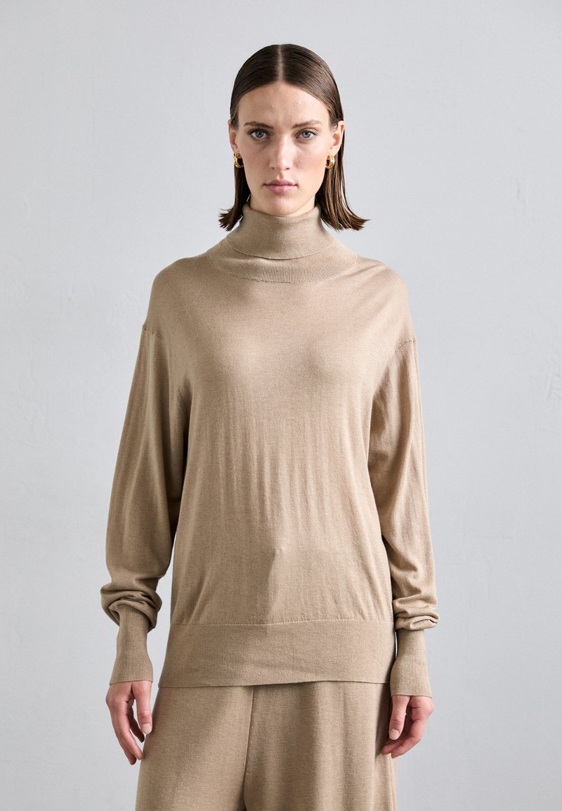Light beige turtleneck sweater with long sleeves, soft texture, and ribbed cuffs. The fit is relaxed and minimalist in design.