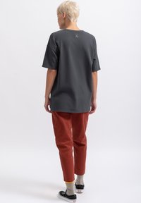Grijze oversized t-shirt met korte mouwen, met een klein scharenlogo op de achterkant. Gecombineerd met nauwsluitende roestkleurige broek en zwarte sneakers.