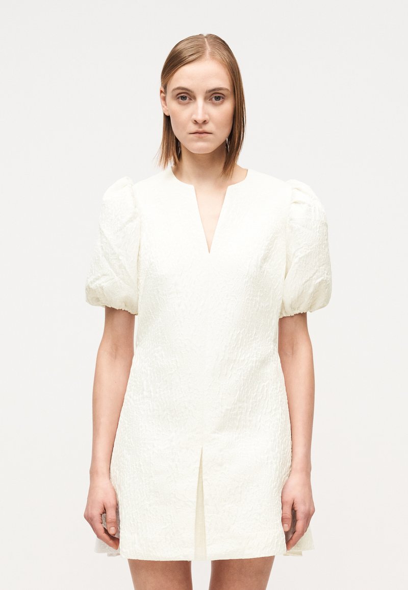 Vestido mini branco com mangas curtas bufantes, tecido texturizado, decote em V e uma fenda frontal. Design simples e justo com acabamento suave.