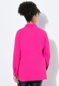 Helles, pinkes, texturiertes Hemd mit Knöpfen, einem Kragen, langen Ärmeln und einem leicht lockeren Schnitt. Verfügt über eine Rückenpasse und Manschetten.