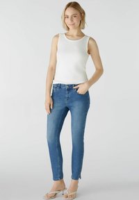 Weißes geripptes Tanktop kombiniert mit blauen Skinny Jeans. Die Jeans haben eine mittlere Bundhöhe und Vordertaschen. Hellbeige Sandalen runden den Look ab.
