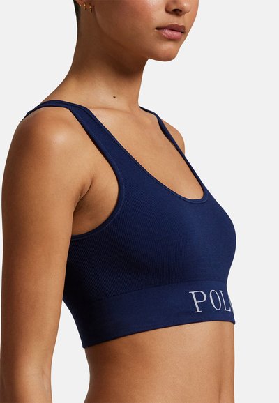 Námornícky modrá rebrovaná športová podprsenka s výstrihom do tvaru výstrihu a širokým spodným lemom, na ktorom je vyšitý nápis "POL" v svetlosivej farbe.
