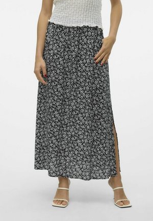 Femme portant une jupe midi florale noire et blanche avec une fente latérale, un top sans manches blanc texturé et des sandales blanches à lanières.